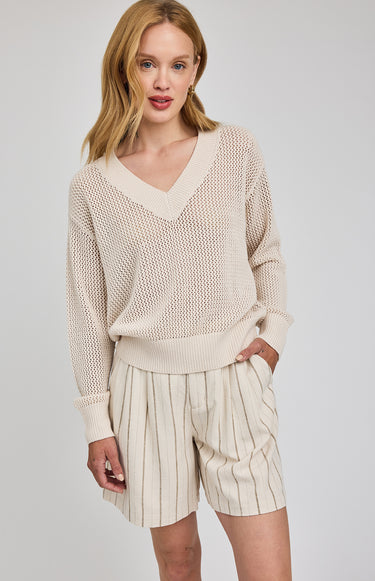 Woman wearing a beige sweater and striped shorts on a plain background
