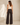A woman shown from the back wearing dark brown wide-leg pants and a cream sleeveless top, standing in a minimalist beige studio setting.