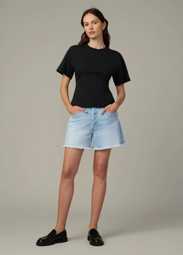 Woman wearing a black t-shirt and light blue denim shorts on a gray background