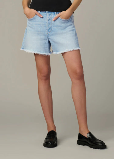 Person wearing light blue denim shorts and black shoes on a neutral background