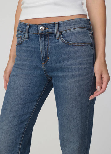 Close-up of a person wearing blue denim jeans with a white cropped top, shown against a light gray studio background.