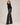 A woman modeling a black long-sleeve crop top and dark charcoal gray wide-leg jeans against a plain light gray studio background.