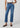 A model wearing a pair of medium-wash blue cropped jeans with a brown belt, paired with a white top and brown slingback flats, against a light gray studio background.