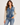 a woman wearing a denim jacket with grey knit sleeves and blue jeans on a white background.
