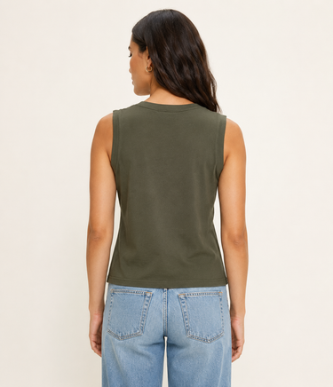 Woman wearing a green sleeveless top and blue jeans on a beige background