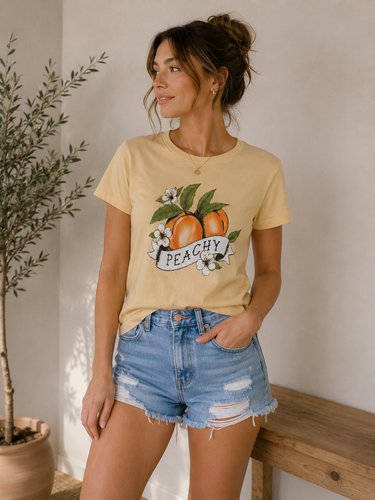 Woman wearing a yellow t-shirt with a peach graphic and 'Peachy' text, standing indoors.