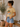 Woman wearing a yellow t-shirt with a graphic design and denim shorts in a home setting.