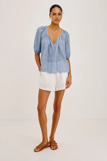 Woman wearing a barletta striped blouse and white shorts on a light gray background