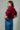 Woman wearing a red blouse and blue jeans against a gray background