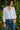 Woman wearing a white blouse and blue jeans standing against a green leafy background