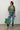 A woman wearing a restructured vintage men’s blouse in olive with a frill collar and blue jeans on a neutral background.