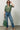 A woman wearing a restructured vintage men’s blouse in olive with a frill collar and blue jeans on a neutral background.