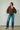 A woman wearing v-neck chocolate sweater and blue jeans and leopard print heels on a neutral background.