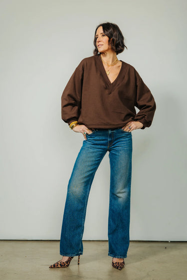 A woman wearing v-neck chocolate sweater and blue jeans and leopard print heels on a neutral background.