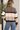 A woman viewed from behind wearing a knit mock-neck sweater with horizontal stripes in taupe, cream, and dark brown, paired with blue jeans.