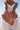 Person holding a brown woven clutch bag on a beach