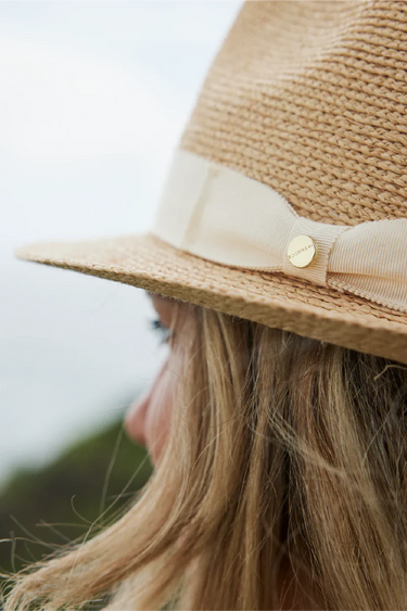 Close-up of a person wearing a straw hat with a ribbon and button, blurred background