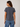 A woman shown from the back wearing a dark gray short-sleeve t-shirt and blue jeans, photographed against a neutral light gray studio background.