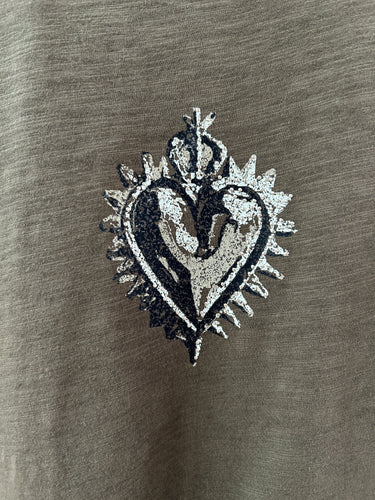A close-up of a metallic silver heart-shaped patch with a distressed, textured finish, placed on a dark gray fabric background.