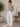 A woman stands in a bright indoor room wearing a light gray short-sleeve t-shirt with small dark star motifs and loose white wide-leg pants.