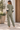 A woman stands outdoors wearing a matching sage green lounge set with white star details on the sleeves and legs, paired with white sneakers.