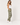 A woman modeling olive green jogger sweatpants with three white embroidered stars down the side, styled with a white tank top and white sneakers against a light gray studio background.
