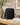 Black leather handbag on a wooden surface with books and a plant in the background
