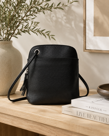 Black leather handbag on a wooden surface with books and a plant in the background