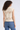 Woman wearing a beige sleeveless knitted top and blue jeans on a white background
