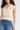 Woman wearing a beige sleeveless knitted top and blue jeans on a white background