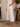 A person wearing white cropped wide-leg pants with thin vertical navy pinstripes, paired with a white sleeveless top and tan flat sandals, standing in a styled indoor setting.
