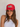 A woman wearing a red trucker-style cap with a white front patch that reads 'Spicy' in green script with a red chili pepper graphic, posed against a light textured wall.
