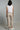 A woman wearing cropped linen beige pants and a white top on a neutral background