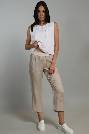 A woman wearing cropped linen beige pants and a white top on a neutral background