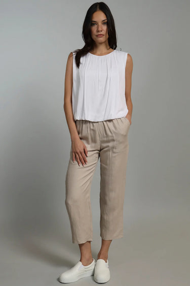 A woman wearing cropped linen beige pants and a white top on a neutral background