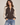 a woman wearing a reversible baseball brown jacket with black jeans on a neutral background.