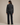 A woman shown from the back wearing a dark charcoal gray fringed denim jacket and matching dark denim jeans against a solid beige studio background.