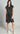 Woman wearing a black sleeveless dress with buttons on a gray background