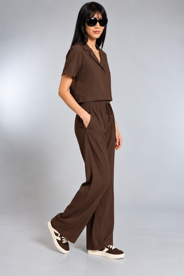 A woman wearing a brown top and satin drawstring brown pants on a white background