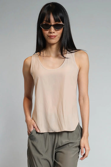 A woman wearing a beige satin tank with a split hem and grey trousers on a studio background.