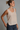 A woman wearing a beige satin tank with a split hem and blue jeans on a studio background.