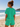 Woman in jade green outfit standing on a beach with ocean view