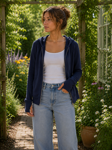 Woman standing in a garden wearing a navy hoodie, white tank top, and light blue jeans.