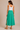 A woman wearing a green Midi skirt and a white tank on a neutral background