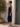 Woman in a navy blue dress standing outdoors next to a white wall and tree.