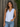 Woman wearing a white sleeveless top with buttons and blue jeans against a wooden background.
