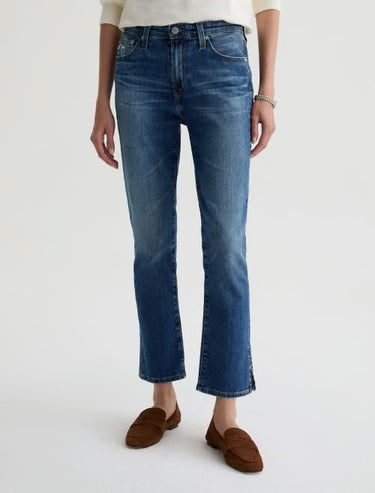 Person wearing blue jeans and brown shoes on a white background