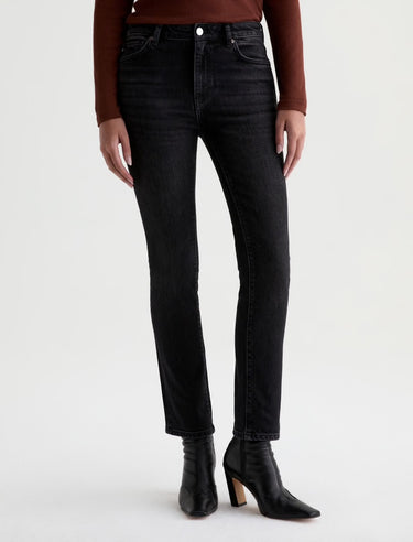 A woman wearing slim straight jeans in black with black boots and a maroon long sleeve tee on a white background.
