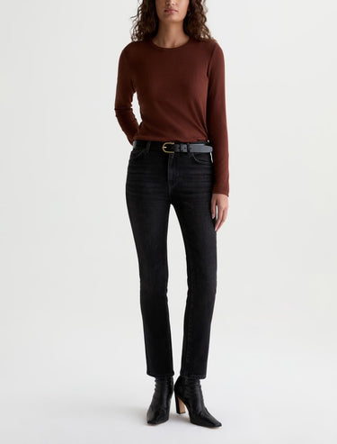 A woman wearing slim straight jeans in black with black boots and a maroon long sleeve tee on a white background.
