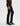 A woman standing sideways wearing slim straight jeans in black with black boots and a maroon long sleeve tee on a white background.